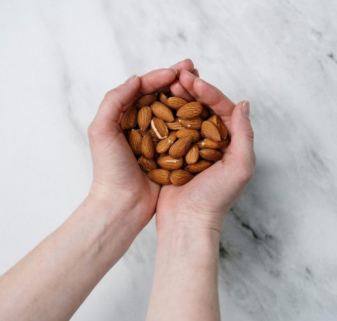 Two hands gently cupping a handful of almonds on a marble background, showcasing healthy snacks.