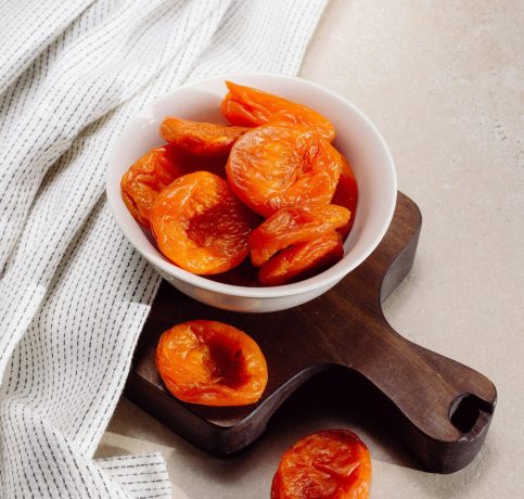 Delicious dried apricots in a white ceramic bowl on a wooden tray, styled for food photography.